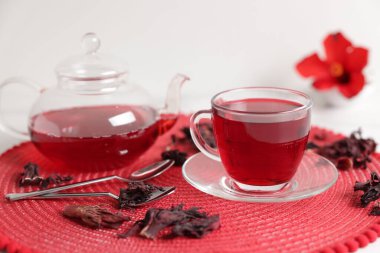 Cam fincanda leziz amber çayı, çaydanlık, kuru roselle sepals ve kaşıklar beyaz masada, yakın plan.