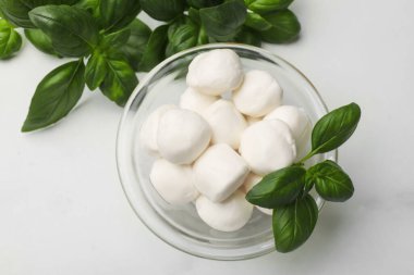 Lezzetli mozzarella peynir topları kasede ve fesleğen beyaz mermer masada, düz yerde.