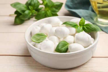 Lezzetli mozzarella peynir topları kasede ve fesleğen açık ahşap masada, yakın plan.