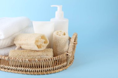 Açık mavi arka planda farklı lif süngerleri, kozmetik ürünleri ve havlular sepette, yakın plan. Metin için boşluk