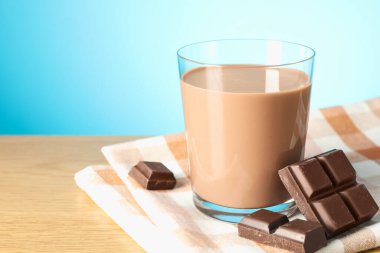 Bardakta çikolatalı süt ve ahşap masada açık mavi arka planda parçalar, yakın plan. Metin için boşluk