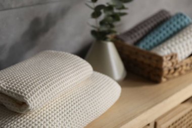 Gri duvarın yakınındaki ahşap şifoniyerde dalları olan waffle havluları ve vazolar.