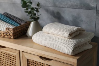 Gri duvarın yanındaki ahşap şifoniyerde dalları olan gözleme havluları ve vazolar.