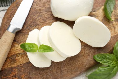 Ahşap masada fesleğen ve bıçakla mozarella peyniri kes.