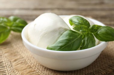 Ahşap masada lezzetli mozzarella peyniri ve fesleğen, yakın plan.