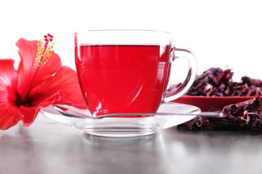 Lezzetli bardakta amber çayı, kuru roselle sepals ve beyaz arka planda gri desenli masada güzel bir çiçek.