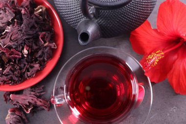 Lezzetli bardakta amber çayı, çaydanlık, kuru roselle sepals ve gri desenli masada güzel çiçek, düz uzanmış