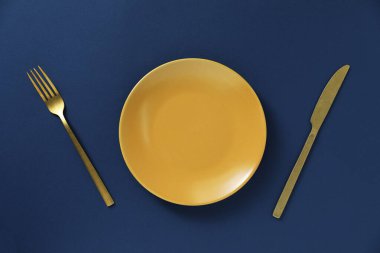 Mavi zemin üzerinde boş tabak ve çatal bıçak takımı, düz yatıyordu.