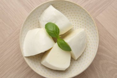 Lezzetli mozzarella peyniri ve fesleğen parçaları ahşap masada, üst tarafta.