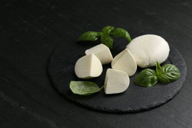 Lezzetli mozzarella peyniri ve fesleğen parçaları koyu dokulu masada, yakın plan.