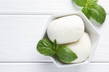 Lezzetli mozzarella peyniri ve fesleğen parçaları beyaz ahşap masada, düz yerde. Metin için boşluk