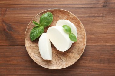 Lezzetli mozzarella peyniri ve fesleğen yaprakları ahşap masanın üstünde.