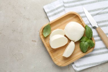 Lezzetli mozzarella peyniri parçaları, fesleğen yaprakları ve gri desenli masa üzerinde bıçak, düz yatak. Metin için boşluk