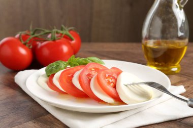 Lezzetli mozzarella, domates, yağ ve fesleğen ahşap masada, yakın plan.