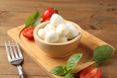 Lezzetli mozarella topları, domatesler ve fesleğenler ahşap masada, yakın plan.