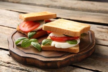Mozarella peynirli, domatesli ve ahşap masadaki fesleğenli lezzetli sandviçler.