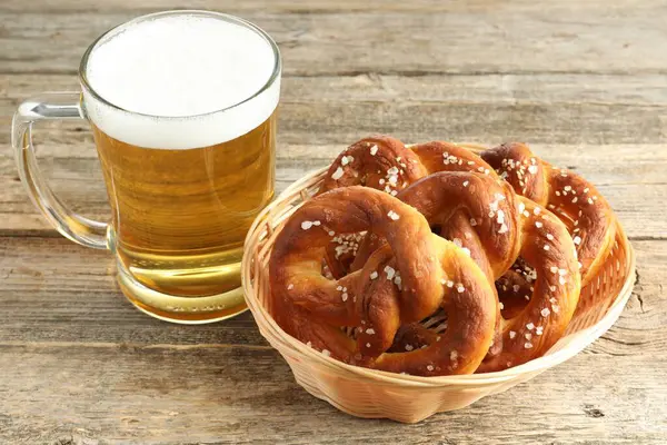Tasty pretzels and glass of beer on wooden table, closeup