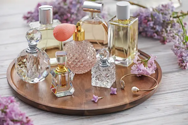 Beyaz ahşap masada, parfüm şişeleri ve leylak çiçekleri, yakın plan.