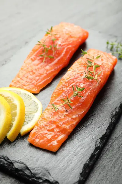 Deniz ürünleri. Somon fileto parçaları, kekik ve limon dilimleri siyah masada, yakın plan.