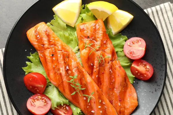 Lezzetli ızgara somon, marul, domates ve limonla servis edilir.