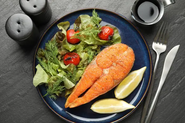 Deniz ürünleri. Siyah masada salata ve limonla servis edilen lezzetli somon bifteği.
