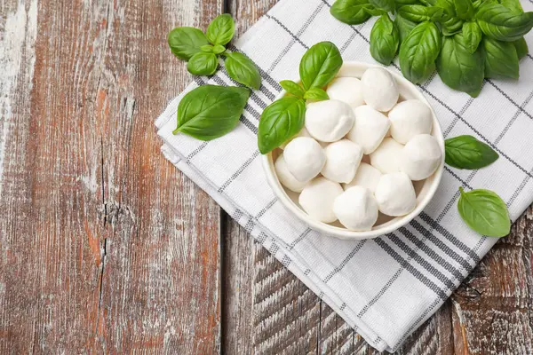 Lezzetli mozzarella peynir topları kasede ve fesleğen tahta masada, düz yerde. Metin için boşluk