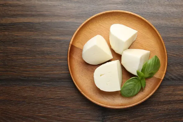 Ahşap masanın üstünde lezzetli mozzarella peyniri ve fesleğen parçaları. Metin için boşluk