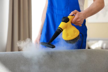 Temizlikçi kanepeyi evde buharlı temizleme makinesiyle temizliyor.