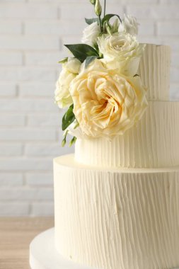 Beyaz tuğla duvarın yanındaki masada çiçeklerle süslenmiş nefis bir düğün pastası.