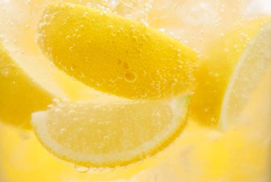 Sarı arka planda limon dilimleri ve buzla soda tazeleniyor. Yakın plan.