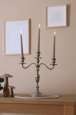 Havalı şamdanlar, yanan mumlar ve bej duvarın yanındaki ahşap masa üzerindeki diğer dekorlar.