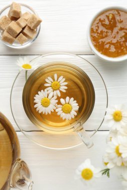 Lezzetli papatya çayı fincanda, kahverengi şeker, çaydanlık, reçel ve taze çiçekler beyaz ahşap masada, düz yatıyordu.