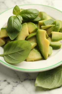 Beyaz mermer masada olgun yeşil avokado ve fesleğen kes, yakın plan.