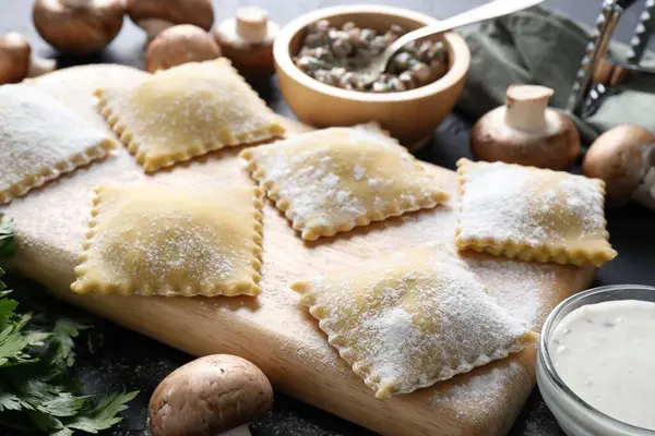 Pişmemiş ravioli ve mantarlar siyah masada, yakın plan.