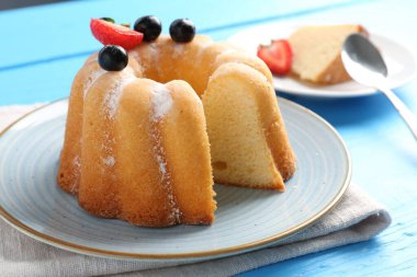 Açık mavi ahşap masada pudra şekerli ve dutlu Lezzetli kek, yakın plan.