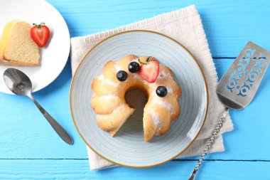 Pudra şekerli ve böğürtlenli lezzetli kek açık mavi ahşap masa, düz uzanmış