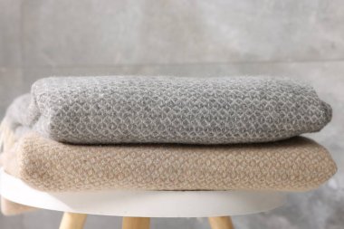 Gri duvarın yanındaki masada katlanmış yün ekose kumaşlar, yakın plan.