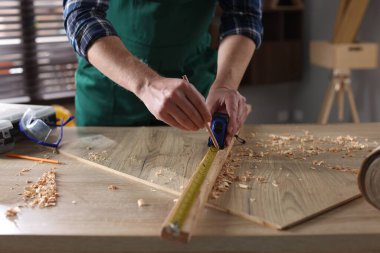 İçerideki ahşap masada bant ile kalas ölçen adam, yakın plan.