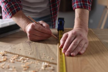 Kapalı alanda bant ile ahşap kalas ölçen bir adam.