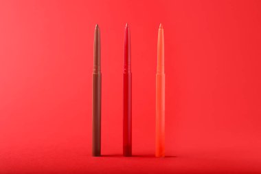 Kırmızı arkaplanda renkli göz kalemleri, yakın plan