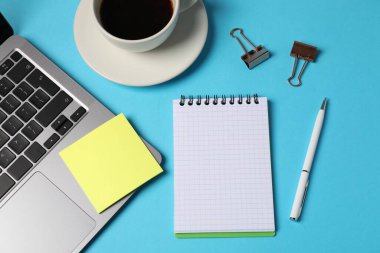 Not defteri, yapışkan not, kalem, cilt klipleri, açık mavi zemin üzerinde kahve ve dizüstü bilgisayar, düz uzanma