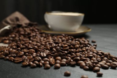 Kahve çekirdekleri ve sıcak içecek siyah masada, yakın plan.