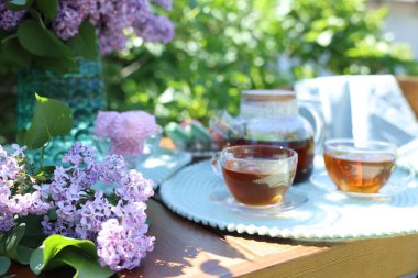 Bahçedeki ahşap masada güzel leylak çiçekleri, tatlılar ve çay, yakın plan.