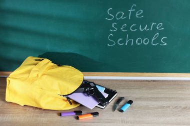 Sırt çantası, silah, bıçak ve kırtasiye tahtanın yanındaki ahşap masada 