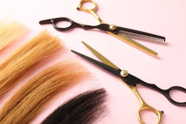 Açık pembe arka planda saç telleri ve kuaför aletleri, yakın plan.