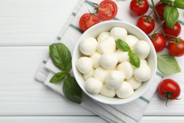 Lezzetli mozzarella peynir topları kasede, fesleğen ve domatesler beyaz ahşap masada, düz yerde
