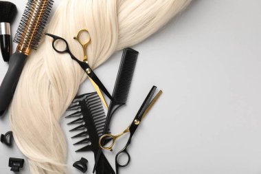 Farklı kuaför aletleri ve açık gri arka planda sarı saç kilidi. Metin için boşluk