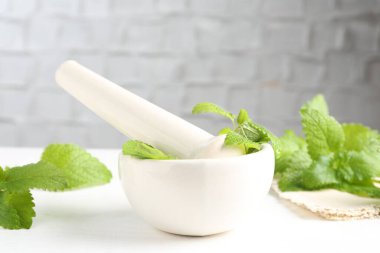 Taze limon merhemi yaprakları ve beyaz ahşap masada havan topuzu, yakın plan.