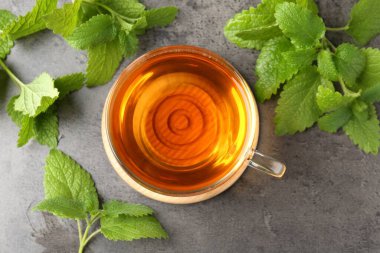 Cam bardakta Aromatik limon merhemi çayı ve gri desenli masada taze yapraklar.