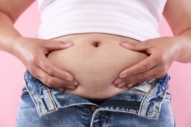 Pembe arka planda göbeği aşırı yağlı bir kadın, yakın plan. Aşırı kilolu